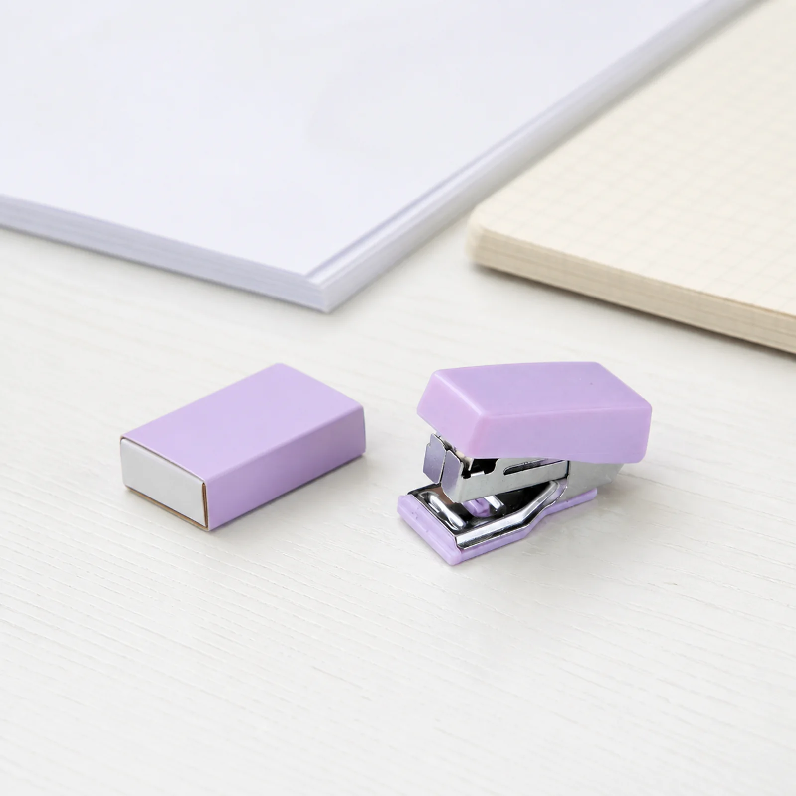 Mini grapadora lila y caja de grapas sobre un escritorio
