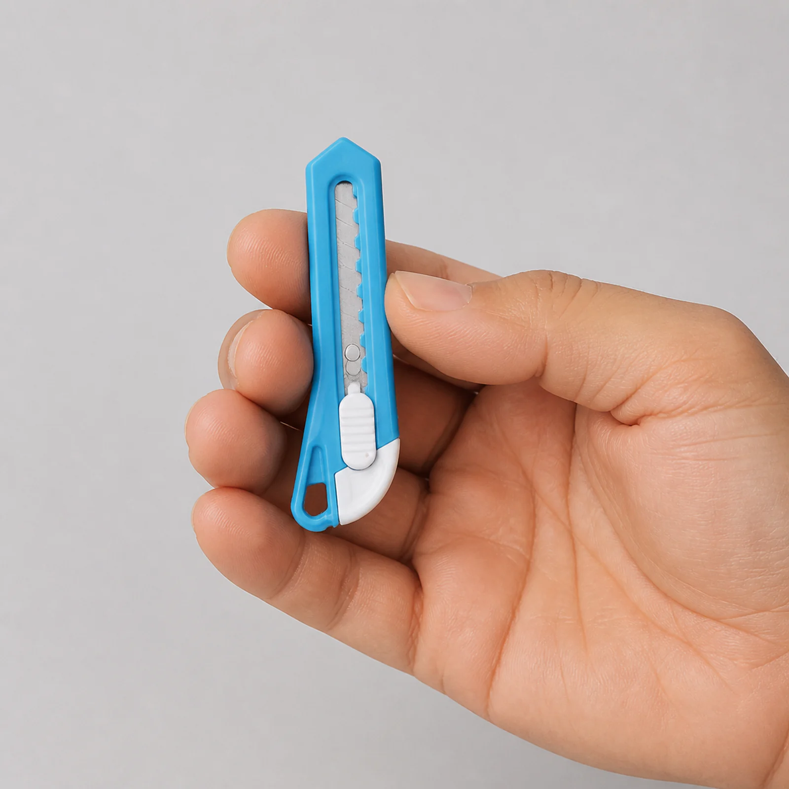 Referencia de escala de mini cortacartón azul sostenido en una mano