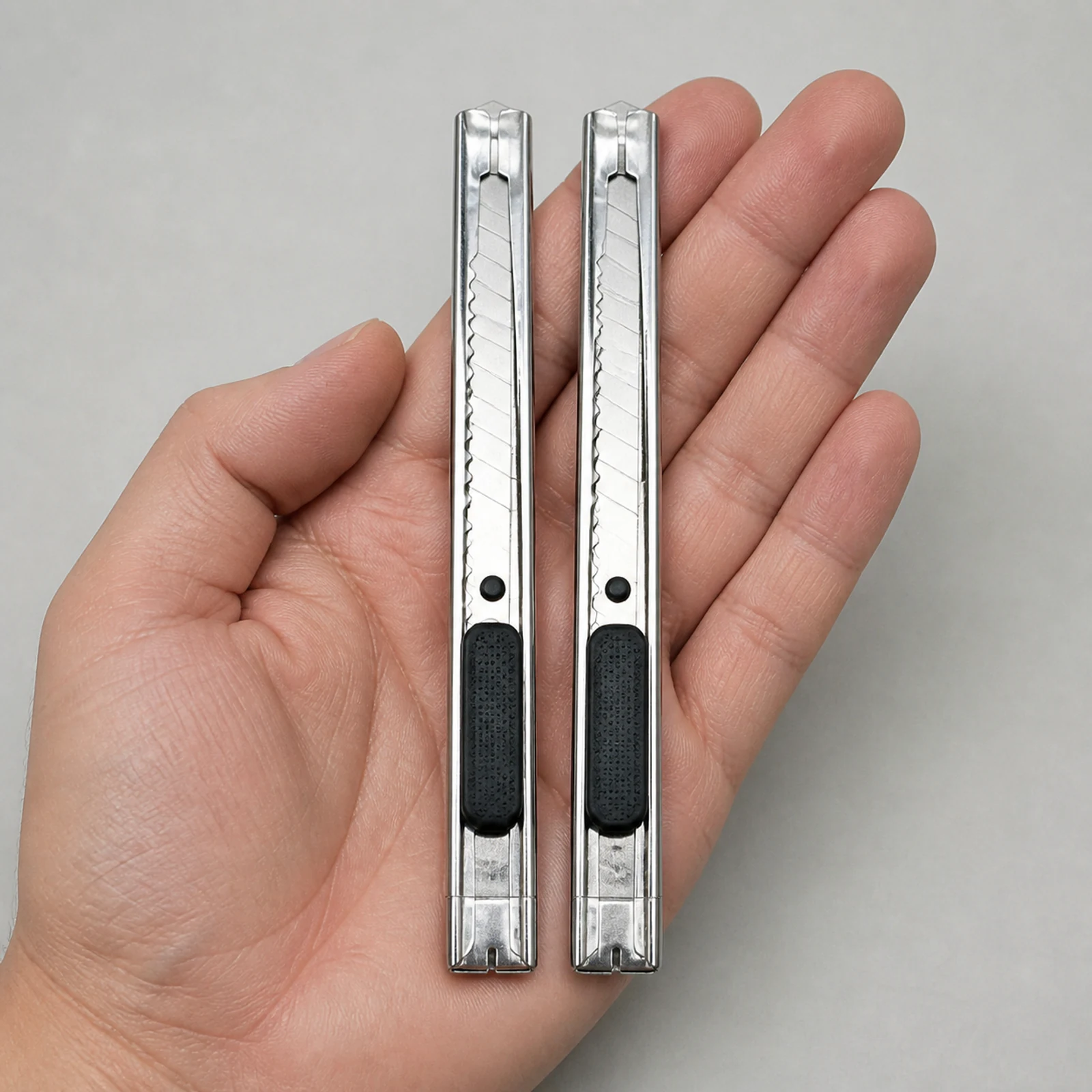 Dos cutters plateados angostos de 9 mm sostenidos en una mano adulta